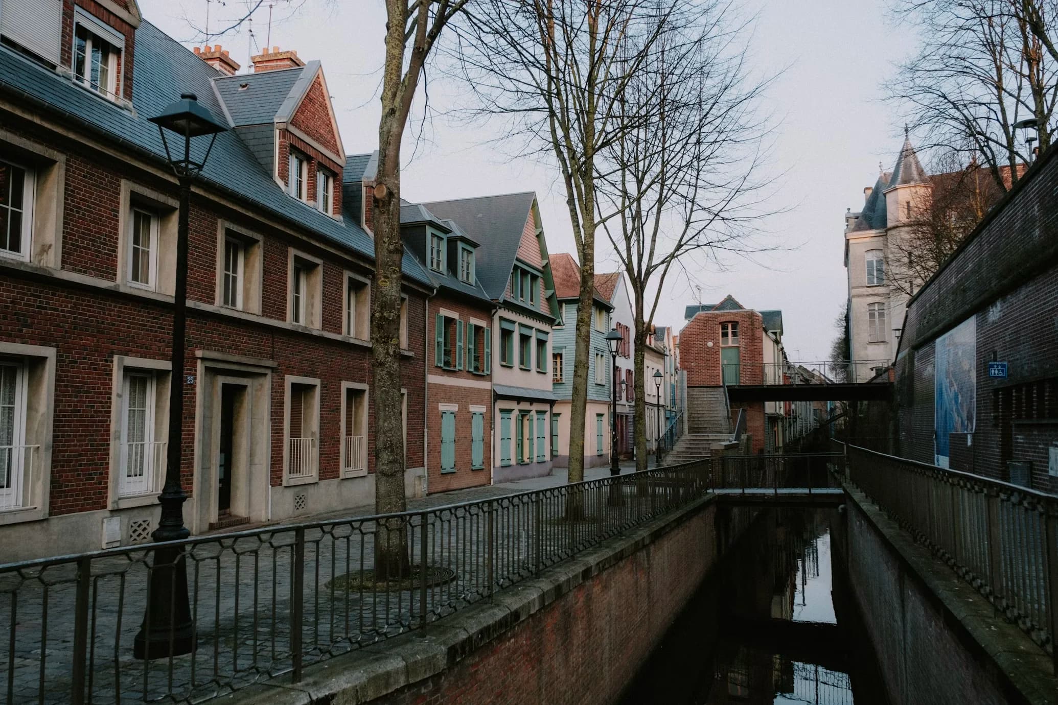 A peaceful canal flows between a row of traditional brick houses and a stone wall.