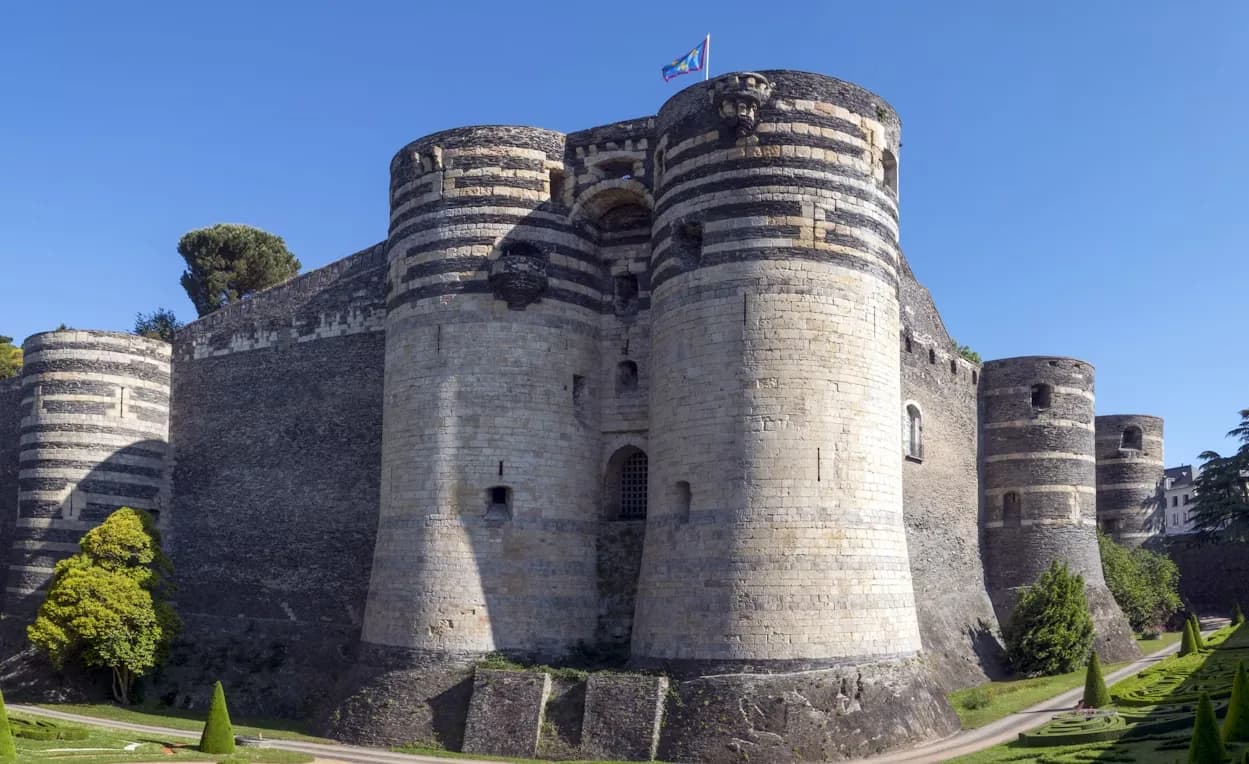 The medieval Château d'Angers, a fortress with imposing striped towers, is surrounded by a moat and well-manicured gardens.