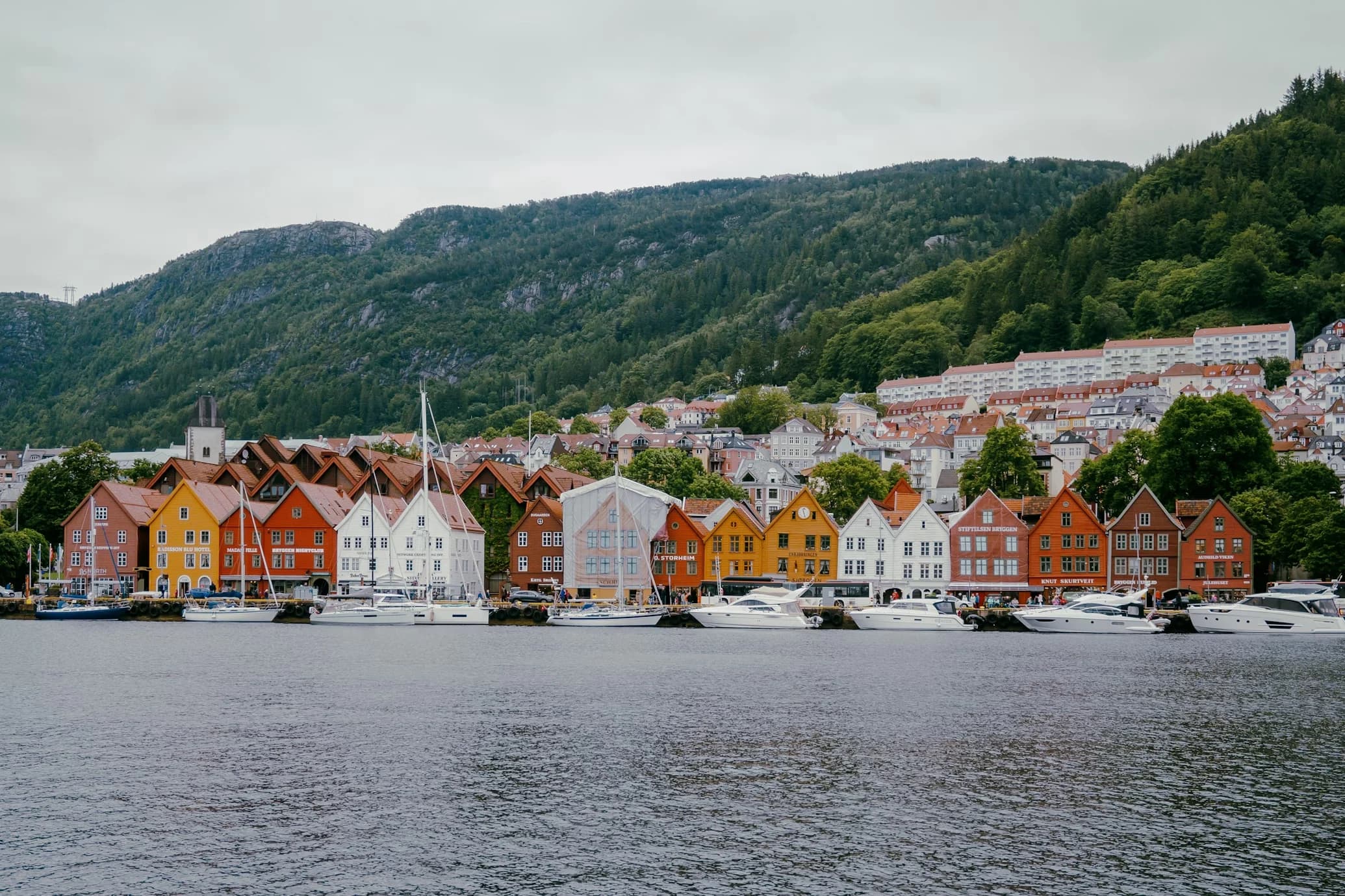 The colorful historic buildings of Bergen's Bryggen Wharf, a UNESCO World Heritage site, are nestled at the base of a lush green hillside.