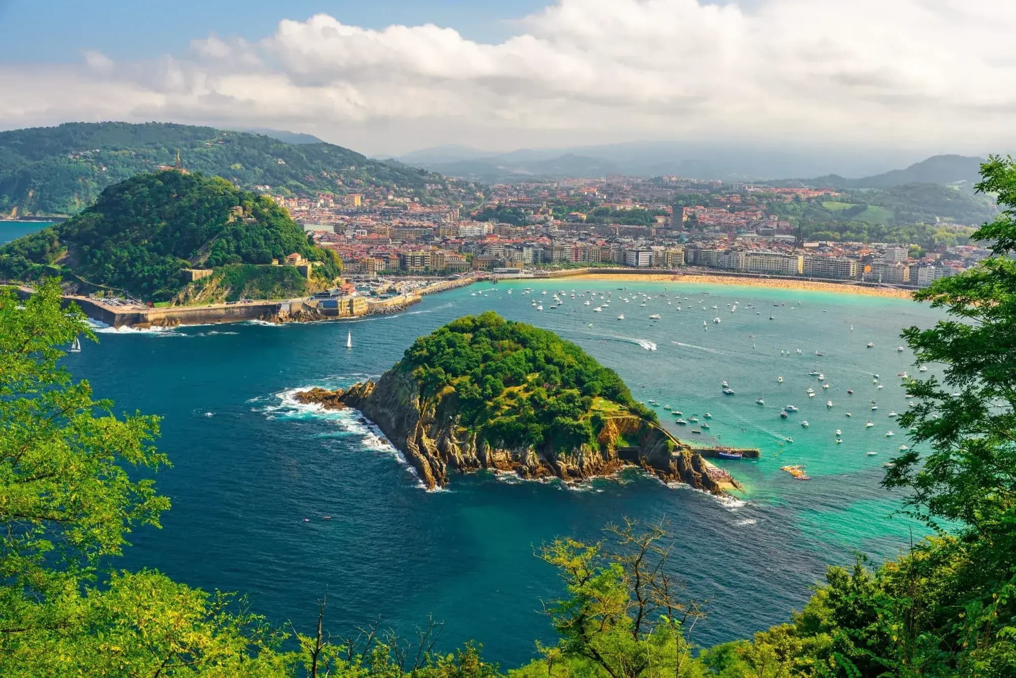 A panoramic view of a beautiful coastal city with a wide bay, surrounded by green hills.
