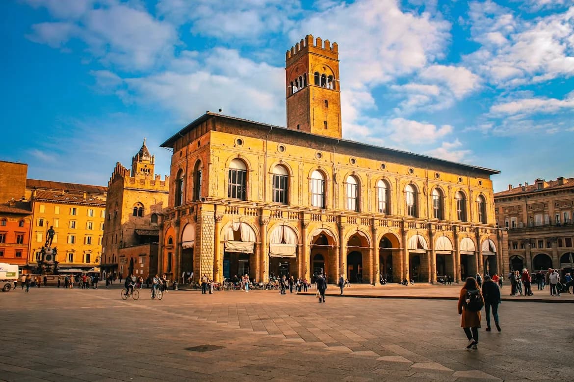 People walk in the vast Piazza Maggiore, with the Palazzo Re Enzo and its soaring brick tower creating a stunning backdrop.
