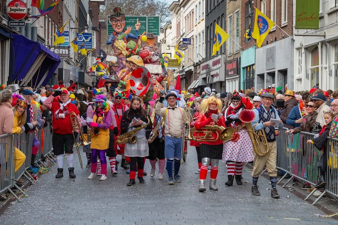 A festive parade with people in colorful costumes, playing musical instruments, marches down a cobblestone street.