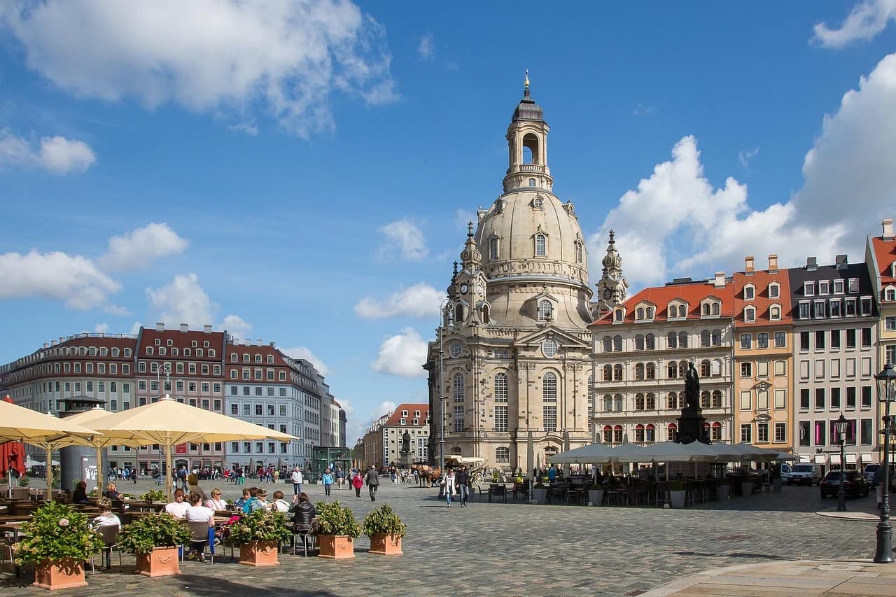The iconic Dresden Frauenkirche stands in the center of a bustling cobblestone square, surrounded by historic buildings and outdoor cafes.