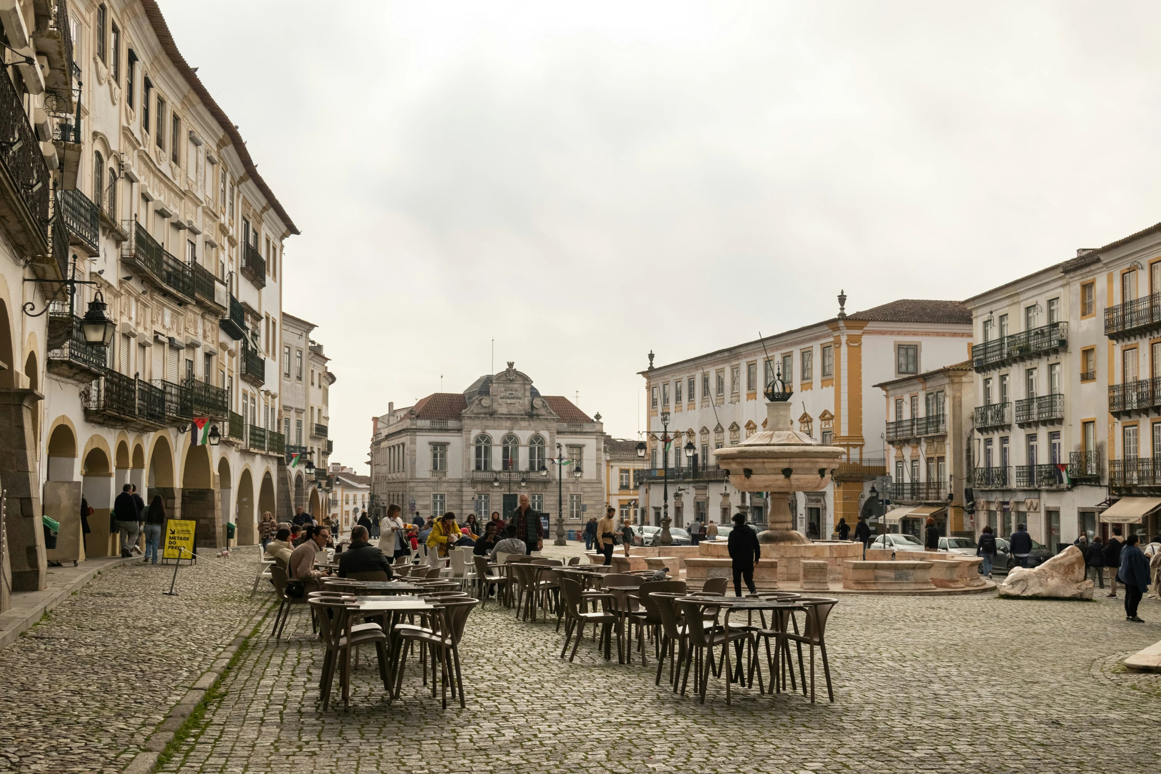 A wide-angle view of Praça do Giraldo in Évora, with outdoor cafes and people seated at tables on the cobblestone square.
