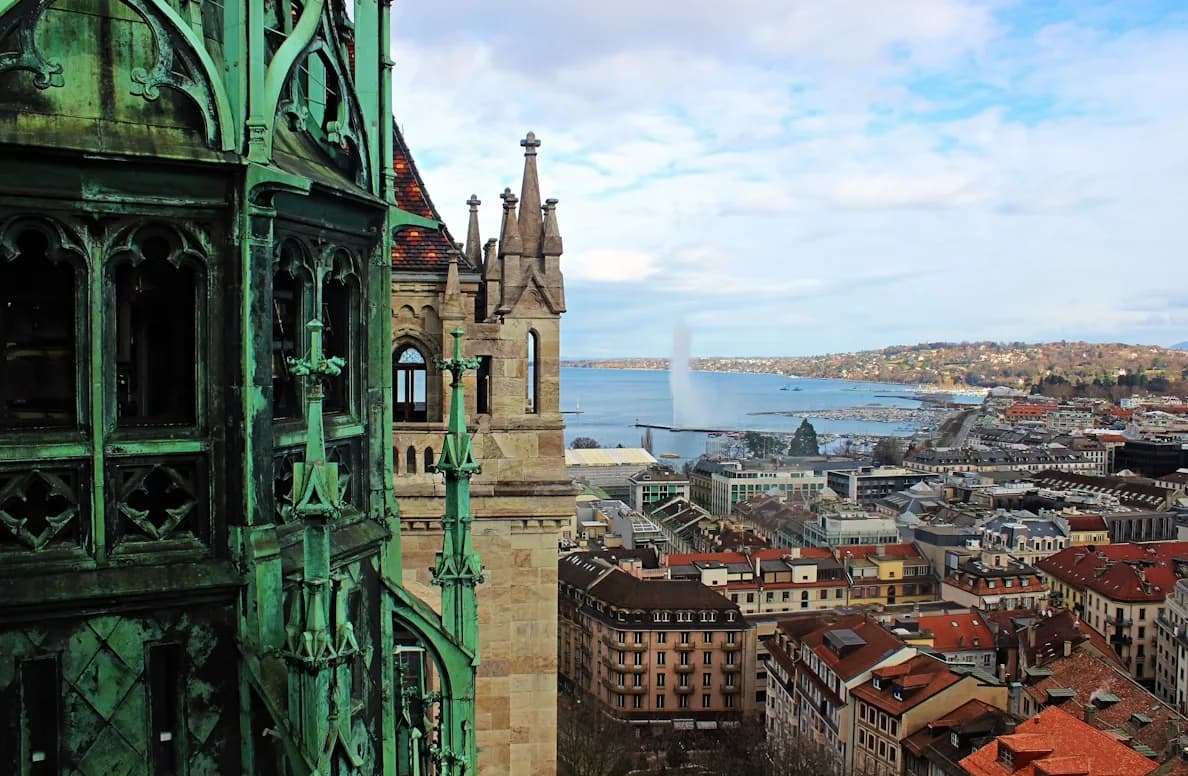 The majestic spires of St. Pierre Cathedral rise above the rooftops of Geneva, with the iconic Jet d'Eau fountain in the distance.