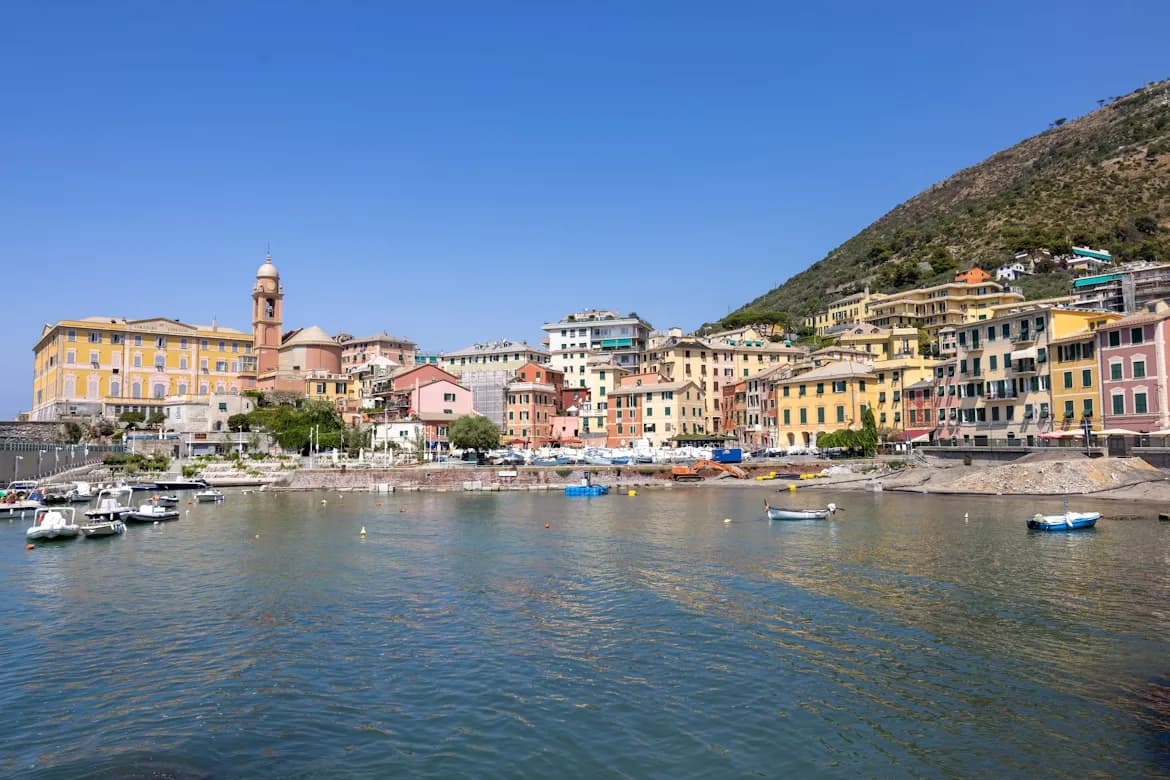 Colorful buildings with traditional red-tiled roofs line the harbor, where fishing boats are moored and a church steeple stands tall on the hill.