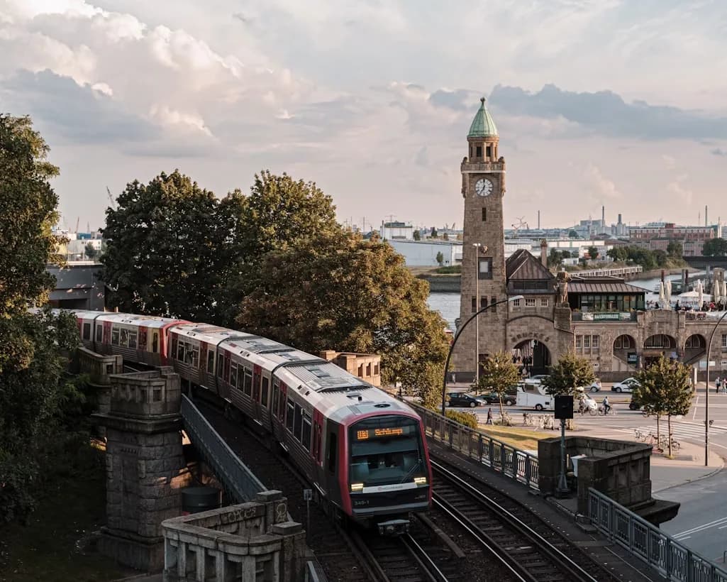 A modern metro train glides past the historic clock tower of the Landungsbrücken, a major transport hub in Hamburg.
