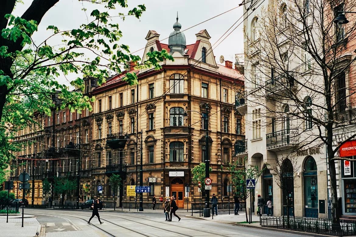 People walk along a street framed by trees and historic buildings in the heart of Krakow.