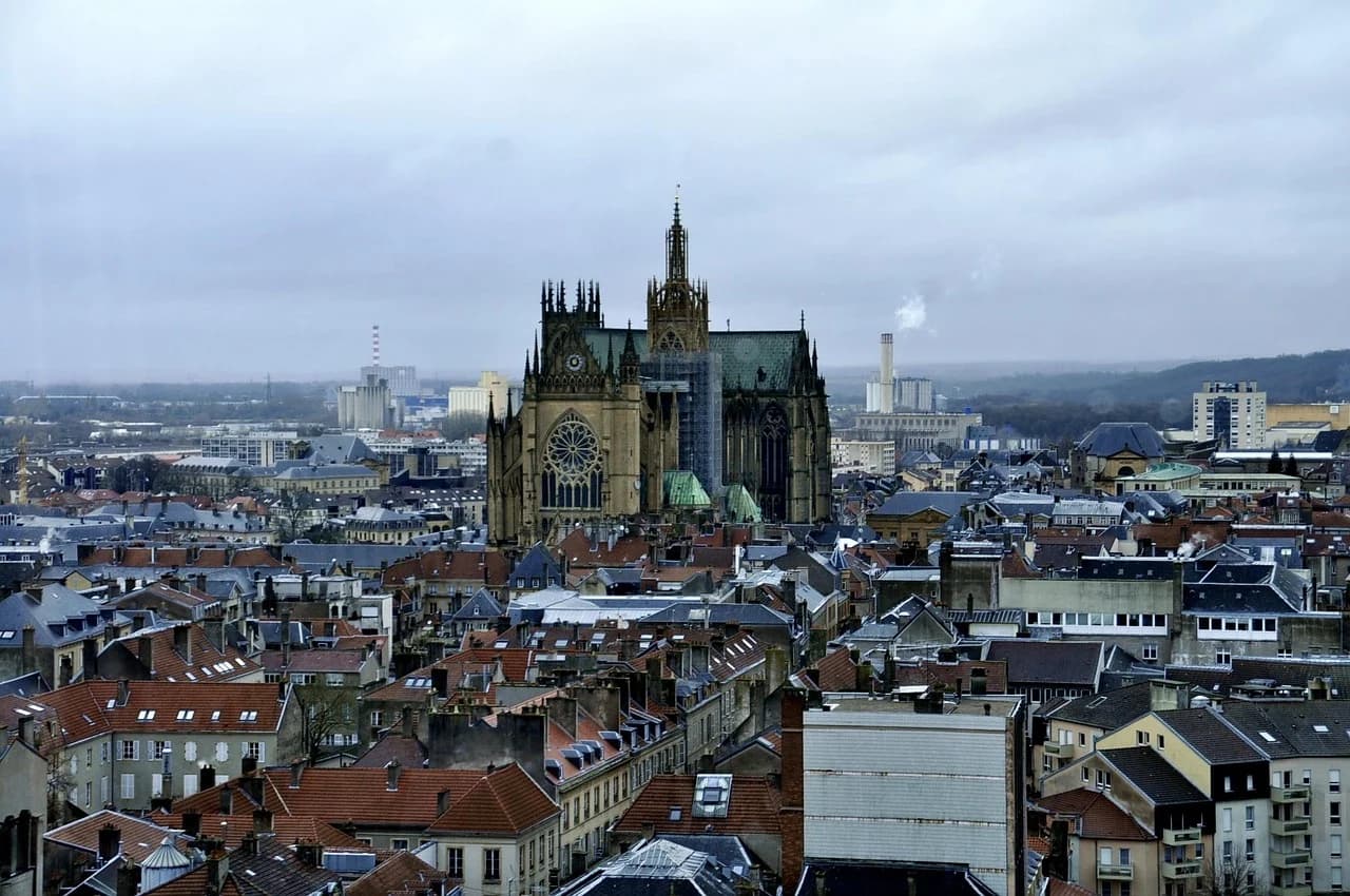 The magnificent Saint-Étienne Cathedral, with its gothic spires and intricate stonework, stands tall above the rooftops of Metz under a cloudy sky.