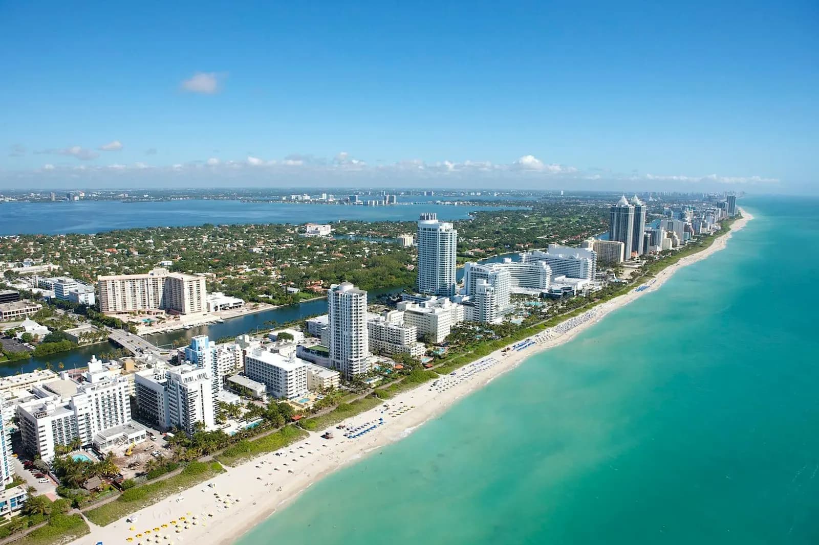 An aerial view captures the vibrant South Beach, with its white sandy beach, turquoise water, and a long line of hotels and resorts.