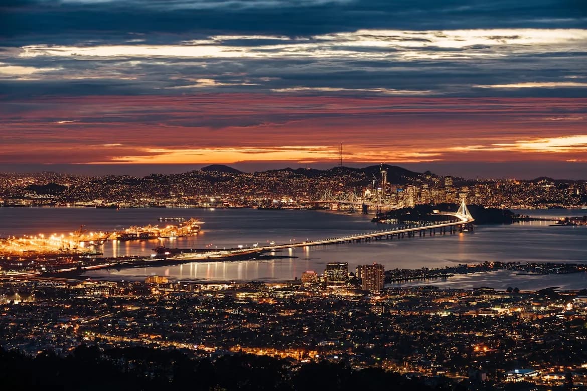 A stunning panoramic view of the Oakland and San Francisco skyline at sunset, with the bridges and city lights glowing.