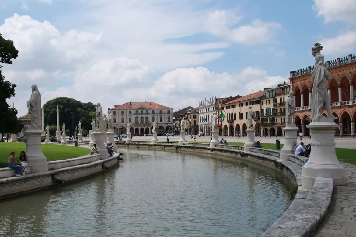 A serene canal with a series of classic statues and bridges flows through the Prato della Valle, a large public square in Padua.