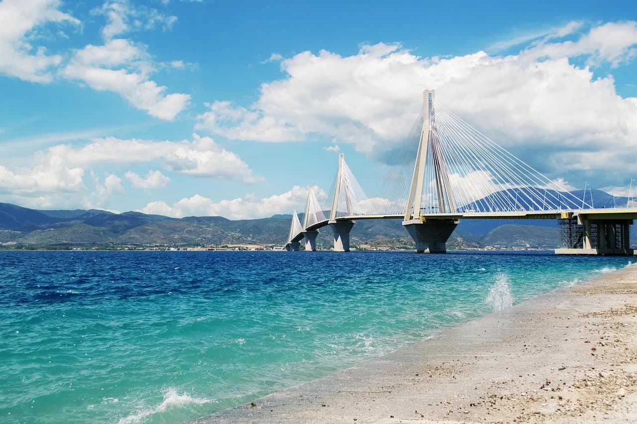 The impressive Rio-Antirrio Bridge, a multi-span cable-stayed bridge, spans a wide river with the mountains in the background.