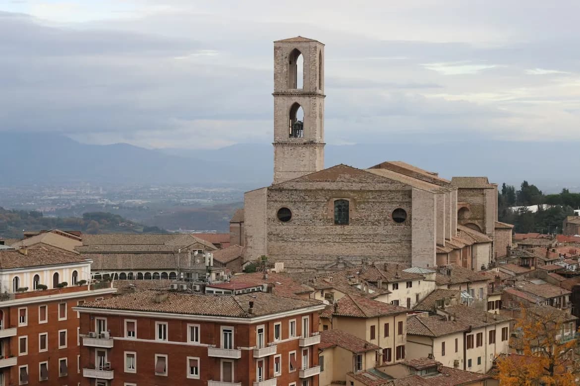 The bell tower of the Basilica di San Domenico rises above the historic red rooftops of Perugia, with distant mountains in the background.