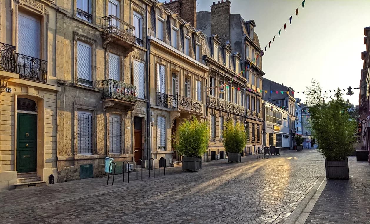A historic city street is lined with elegant, traditional buildings with long windows and iron balconies.