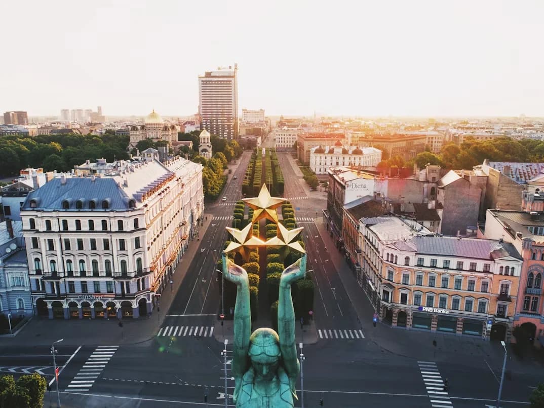 The Freedom Monument, with a statue of a woman holding three stars, stands in a wide, tree-lined boulevard in Riga.