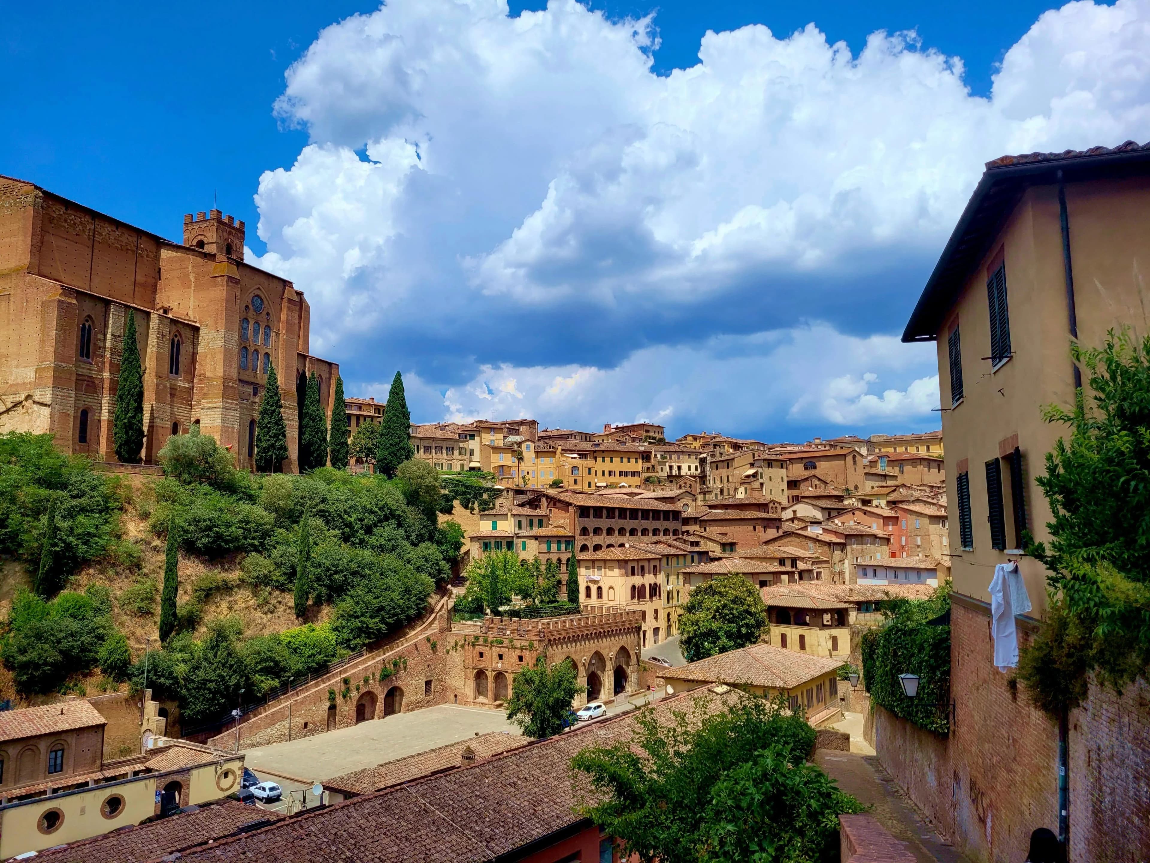 A narrow, cobblestone alleyway winds between historic buildings in Siena's Old Town, with a few small cafes and shops.