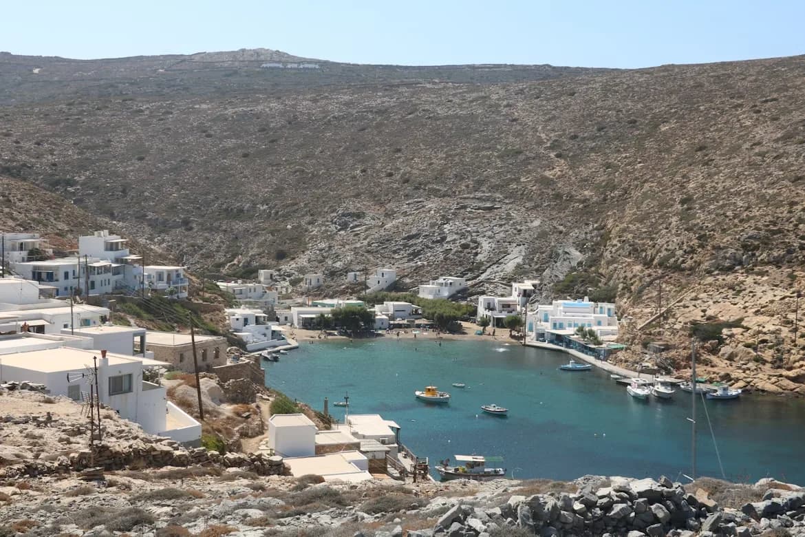 A small, quiet bay is surrounded by traditional white-washed buildings and rocky hillsides.