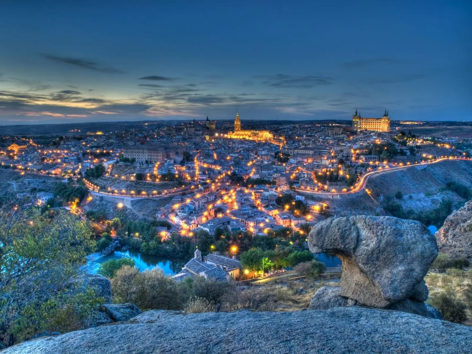 An aerial view captures the historic fortified city of Toledo, a UNESCO World Heritage site, perched on a hill surrounded by a river.