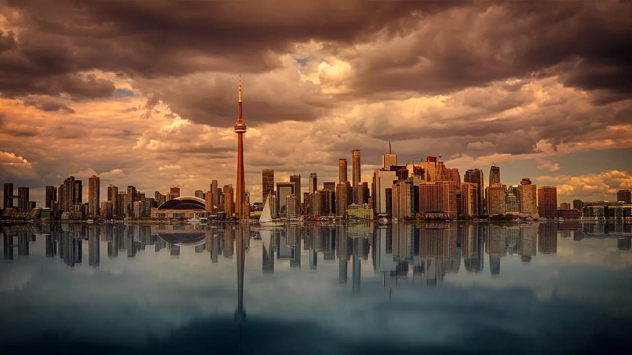 The illuminated Toronto skyline is a stunning sight at night, with the CN Tower and modern skyscrapers reflected in the calm waters of the Lake Ontario.