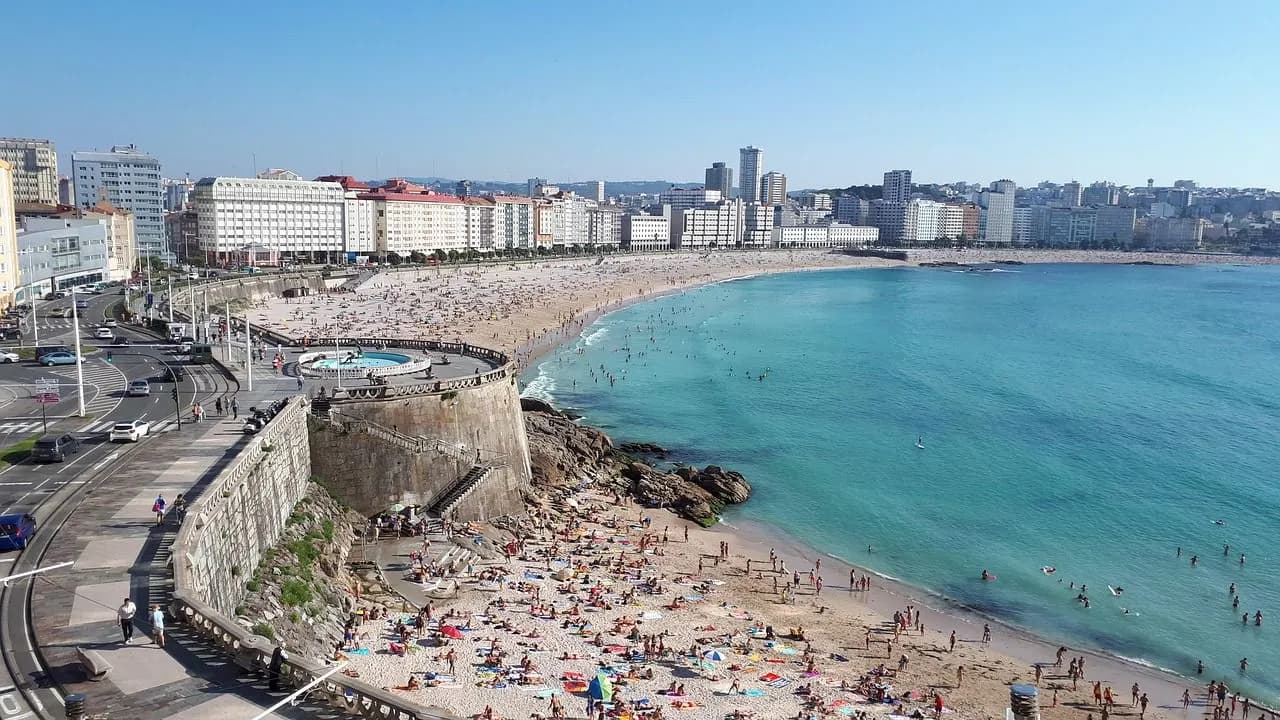 Curved sandy beach of A Coruña bordered by turquoise Atlantic waters and the city’s vibrant seaside promenade.