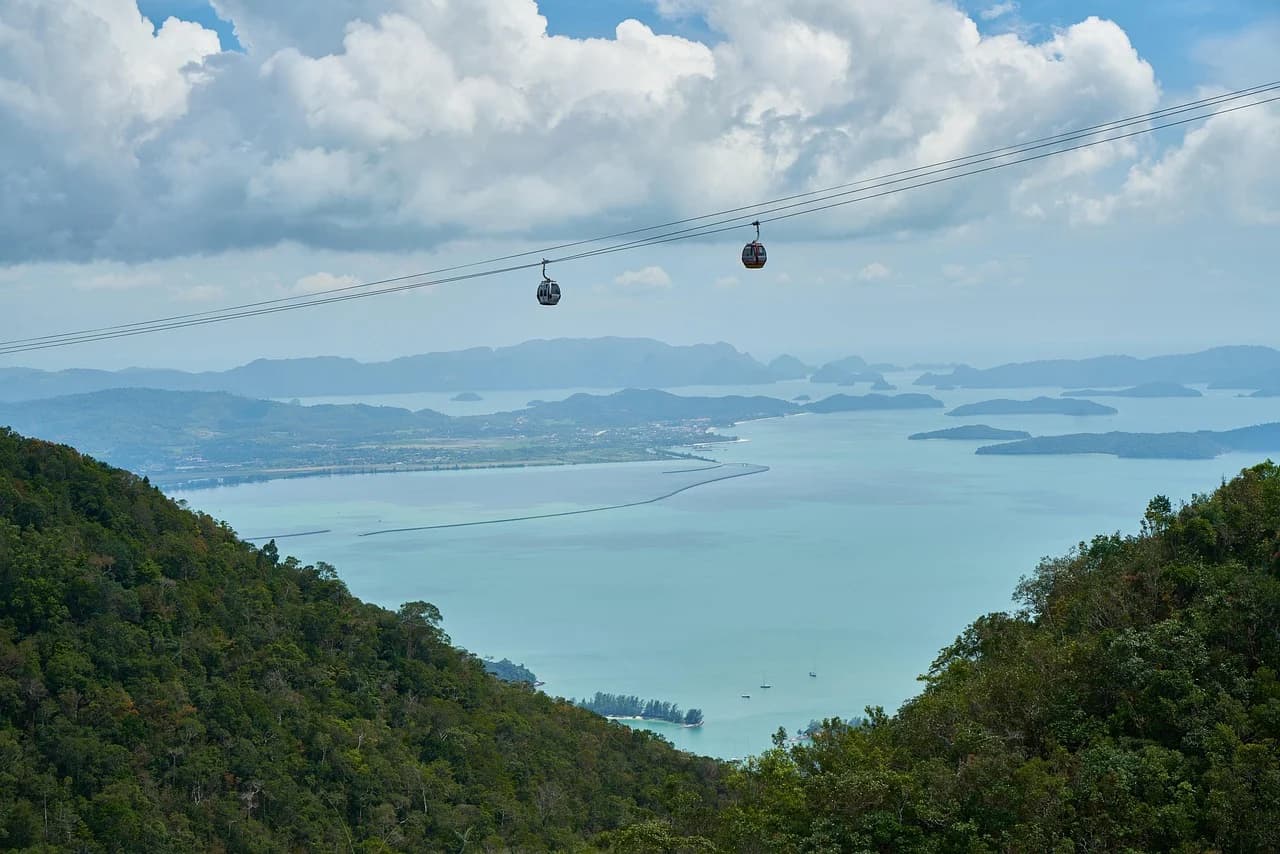 Cable cars travel over a lush green valley with a vast lake and distant islands, offering a breathtaking view.