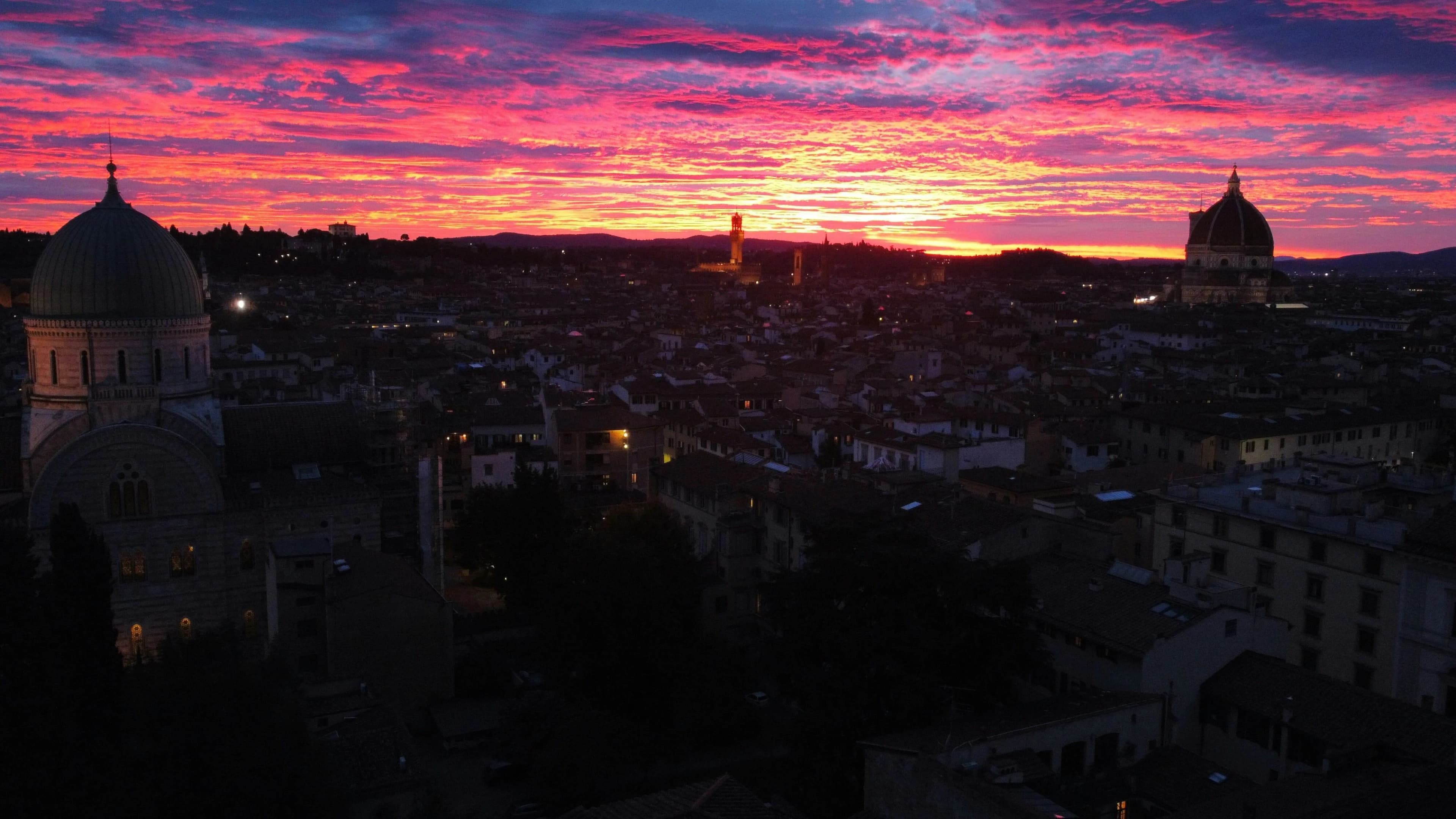 The skyline of Aix-en-Provence is silhouetted against a breathtakingly vibrant sunset of pinks and reds.