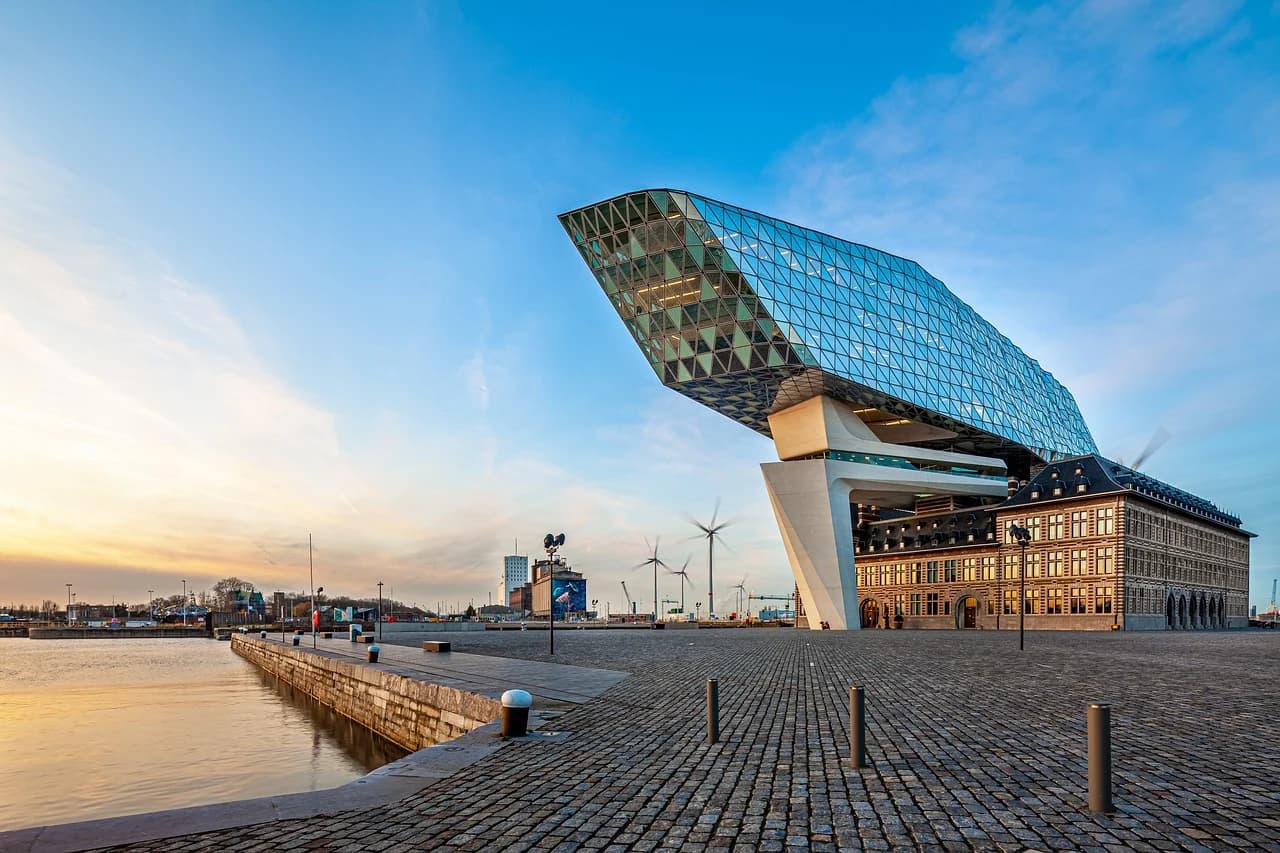 The stunning Port House, with its modern diamond-like structure, sits on a stone quay next to a historic building at dusk.