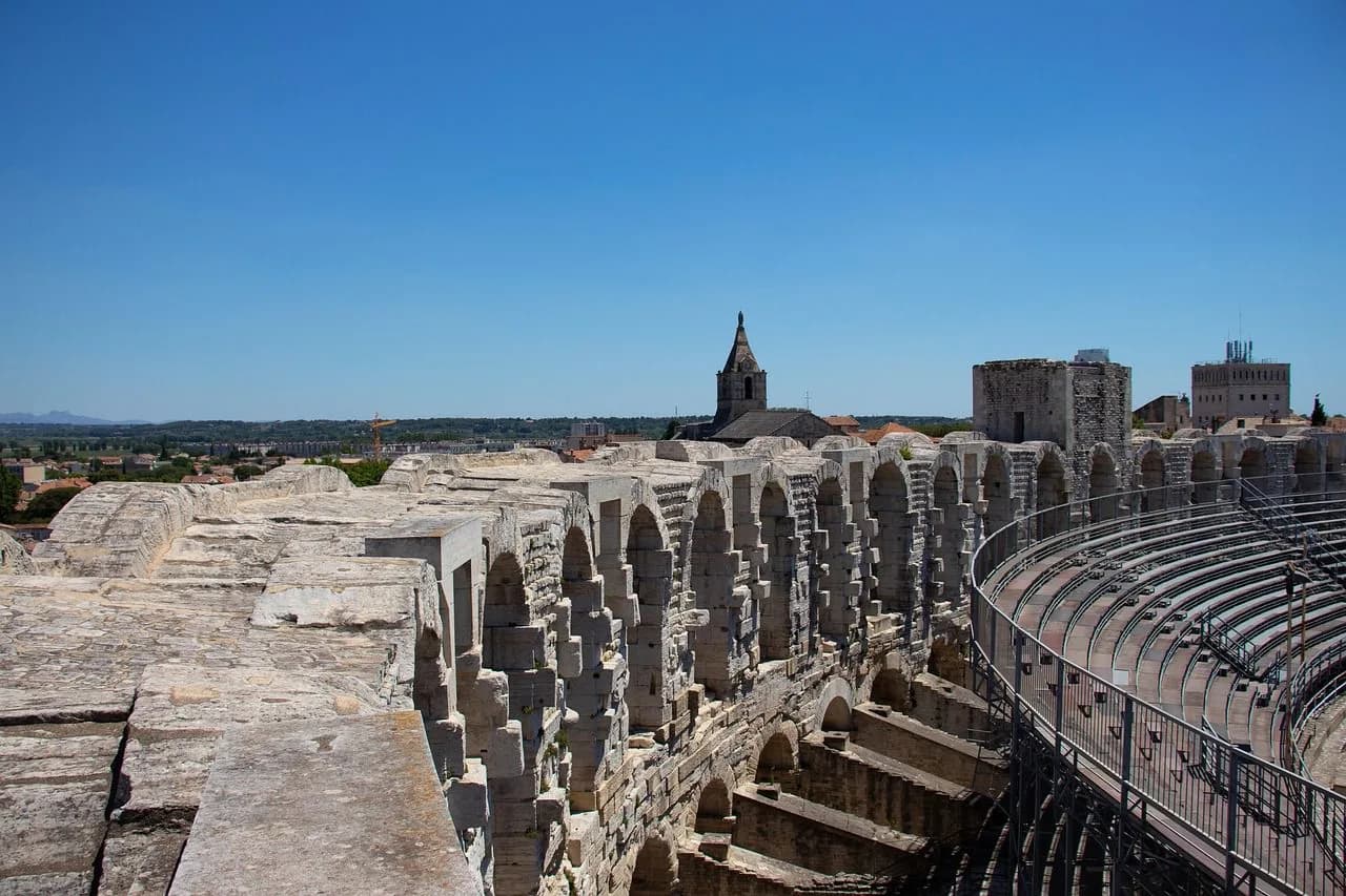 A view from the top of the Roman Amphitheatre of Arles shows the rows of seats and the historic buildings of the city.