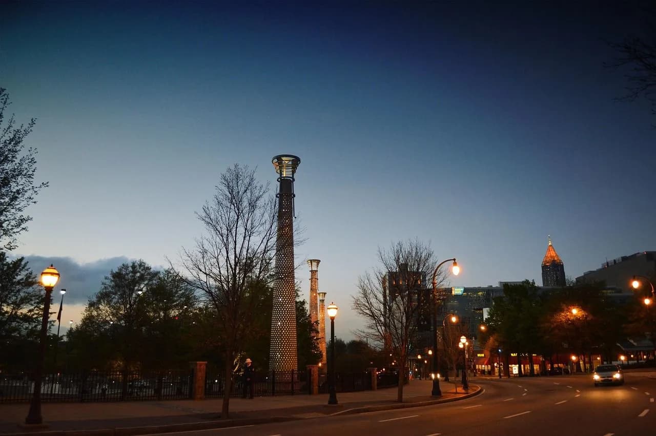 A line of unique, light-up street lamps illuminates a quiet city street at night, with a modern skyscraper in the distance.