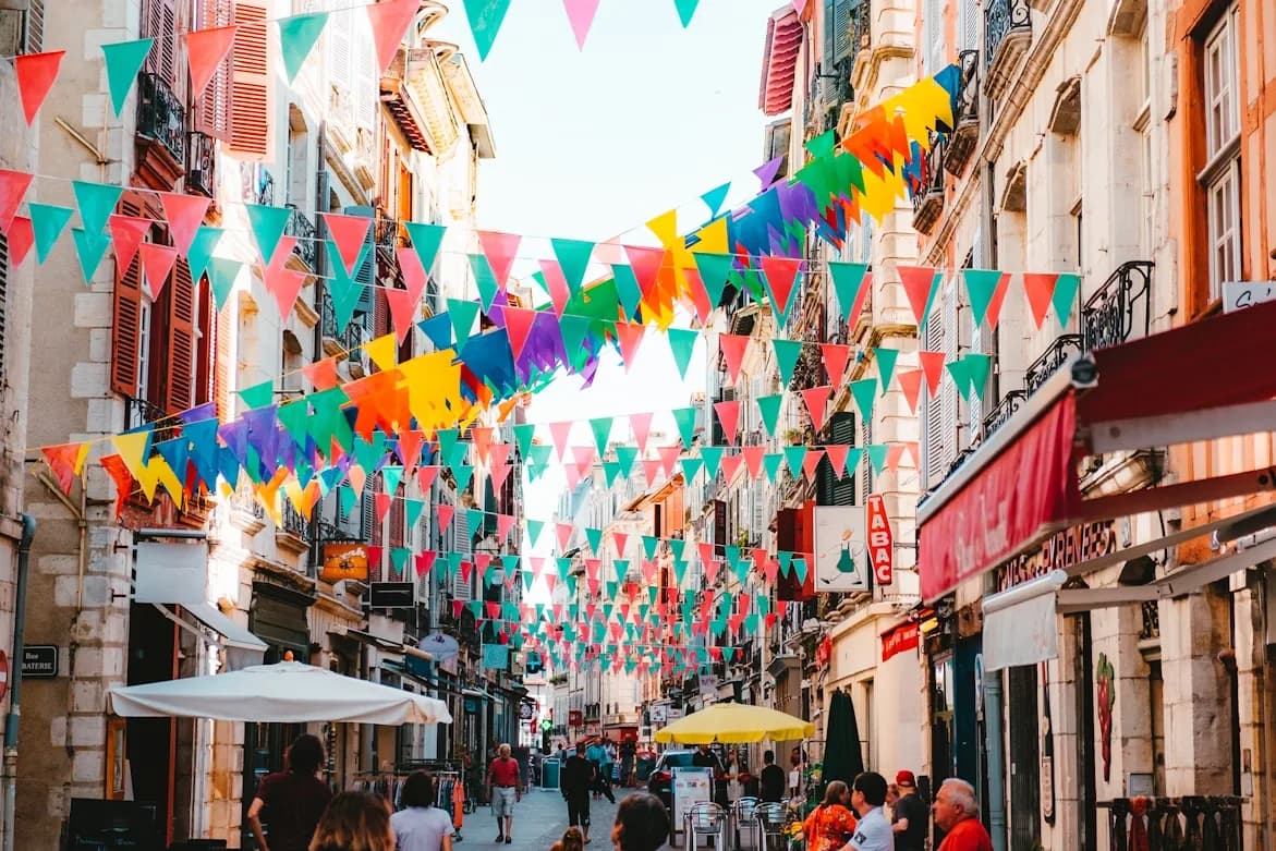 A festive street in Bayonne is decorated with bright, colorful pennants and is lined with historic buildings and bustling cafes.