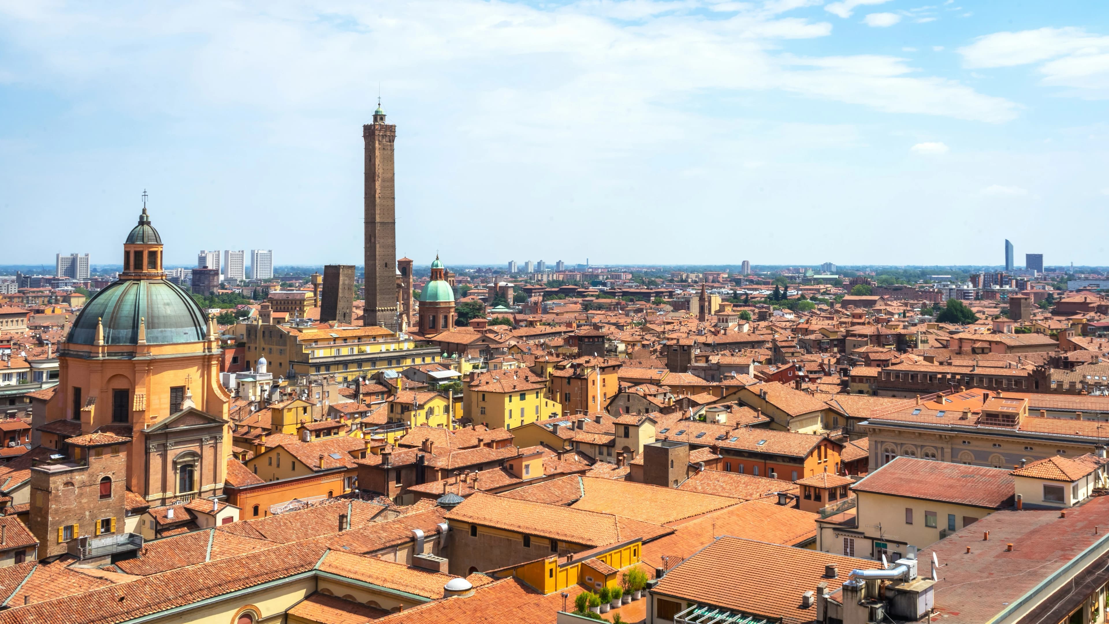 An aerial view captures the dense cluster of red rooftops and historic domes that define Bologna's cityscape.