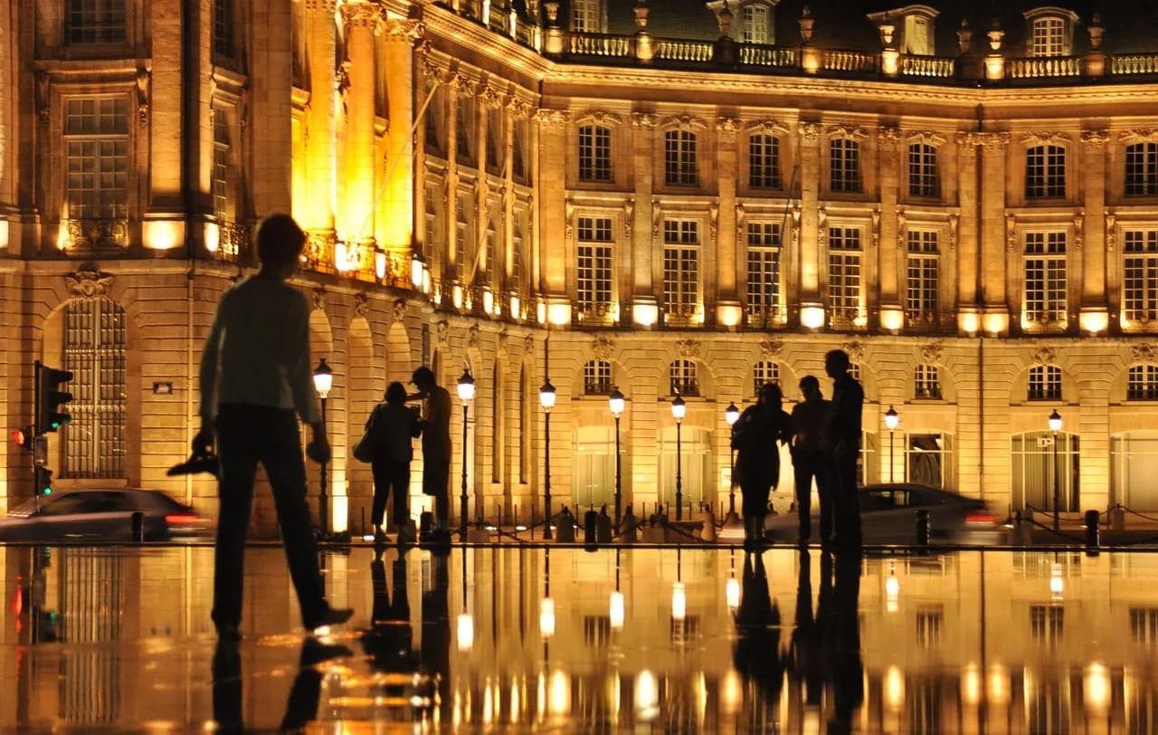 The elegant buildings of the Place de la Bourse are beautifully illuminated at night and reflected in the water-covered plaza.