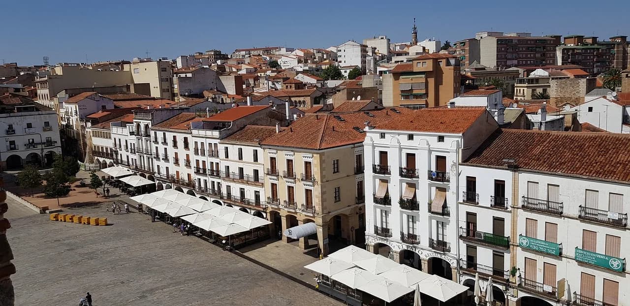 A wide view of a city square shows traditional buildings with arched walkways and outdoor seating.