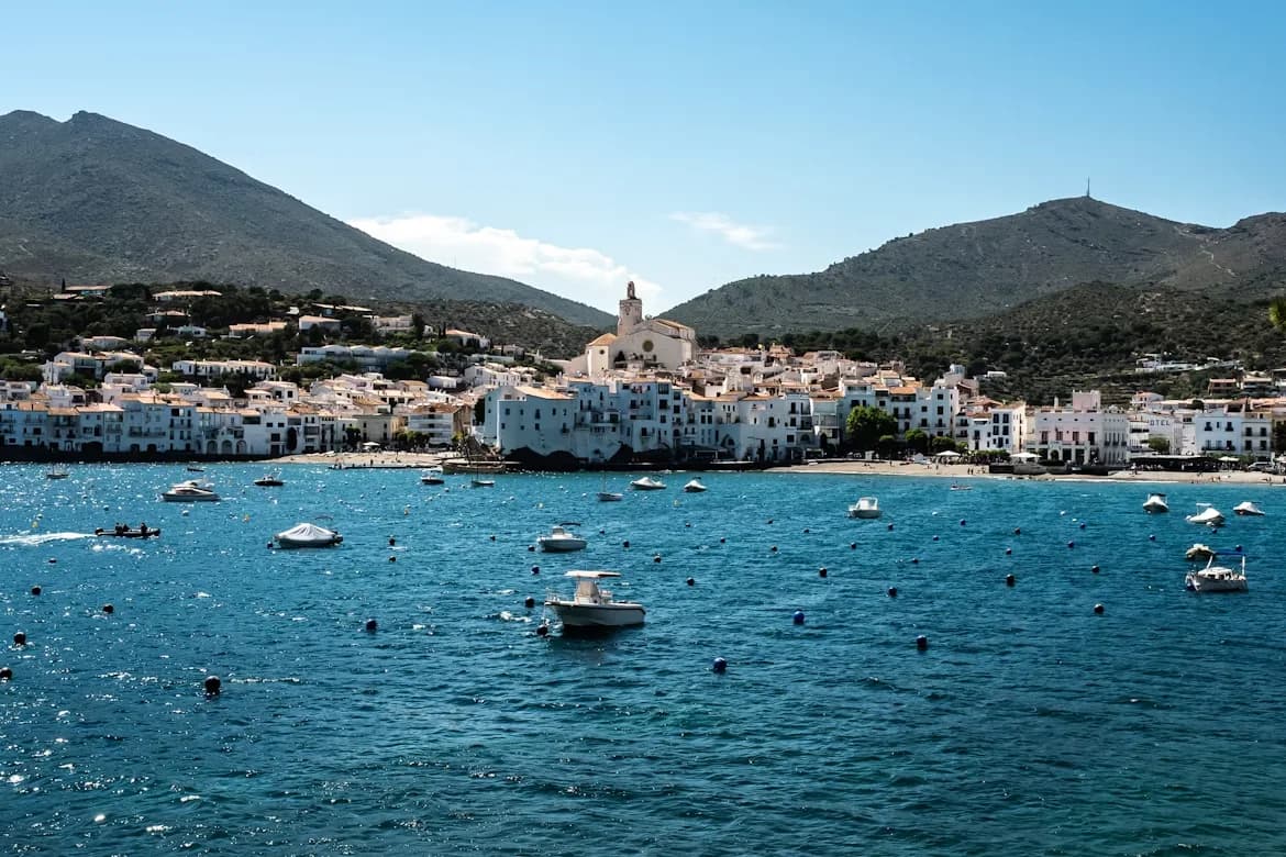 The stunning white buildings of Cadaqués are clustered around a picturesque bay, with numerous boats anchored in the water.