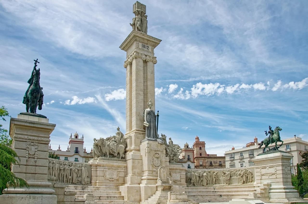 The Monument to the Cortes of Cádiz, a grand monument with statues and columns, stands in a sunlit square.