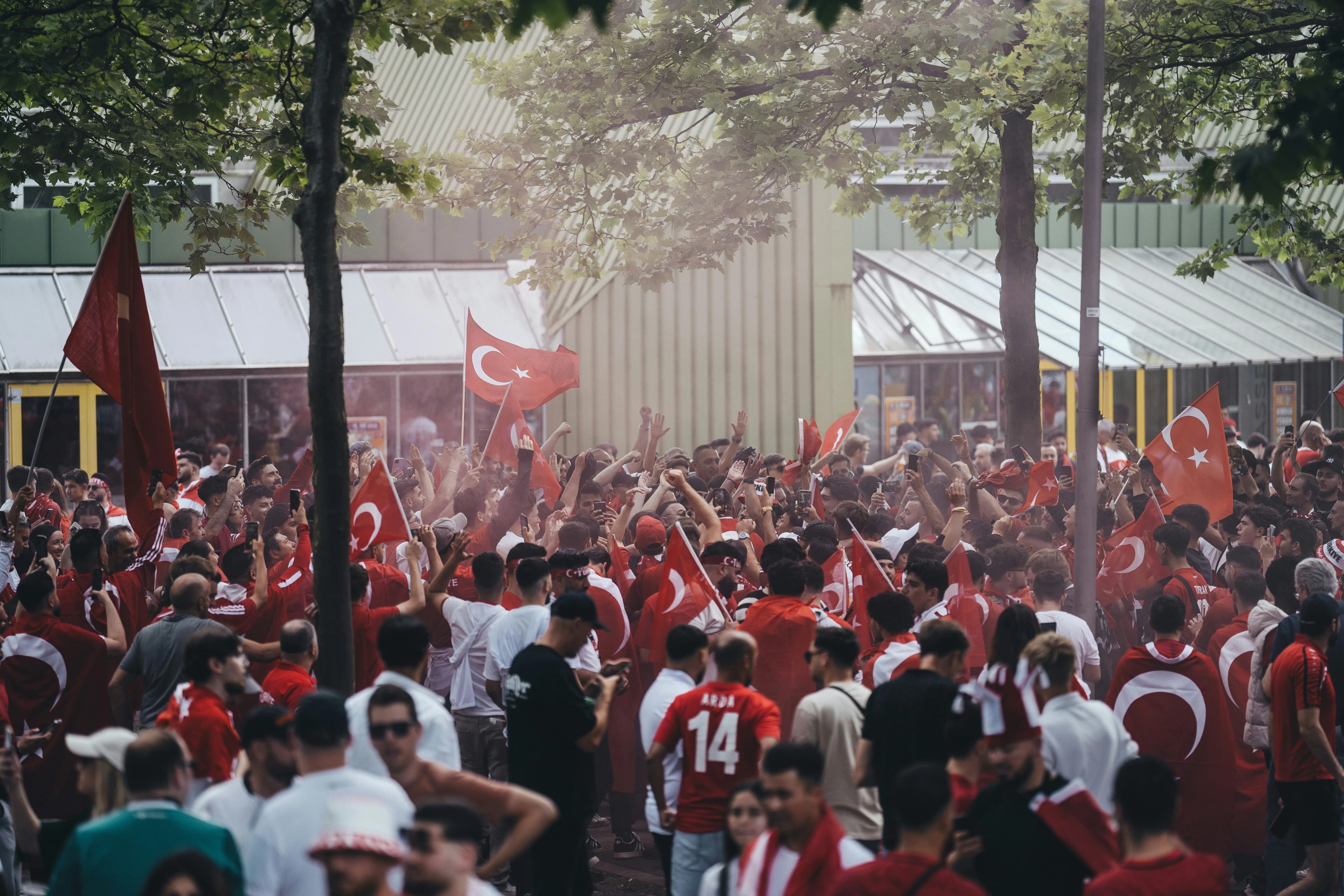 A large crowd of people, many holding flags, gathers for a public event in a city square.