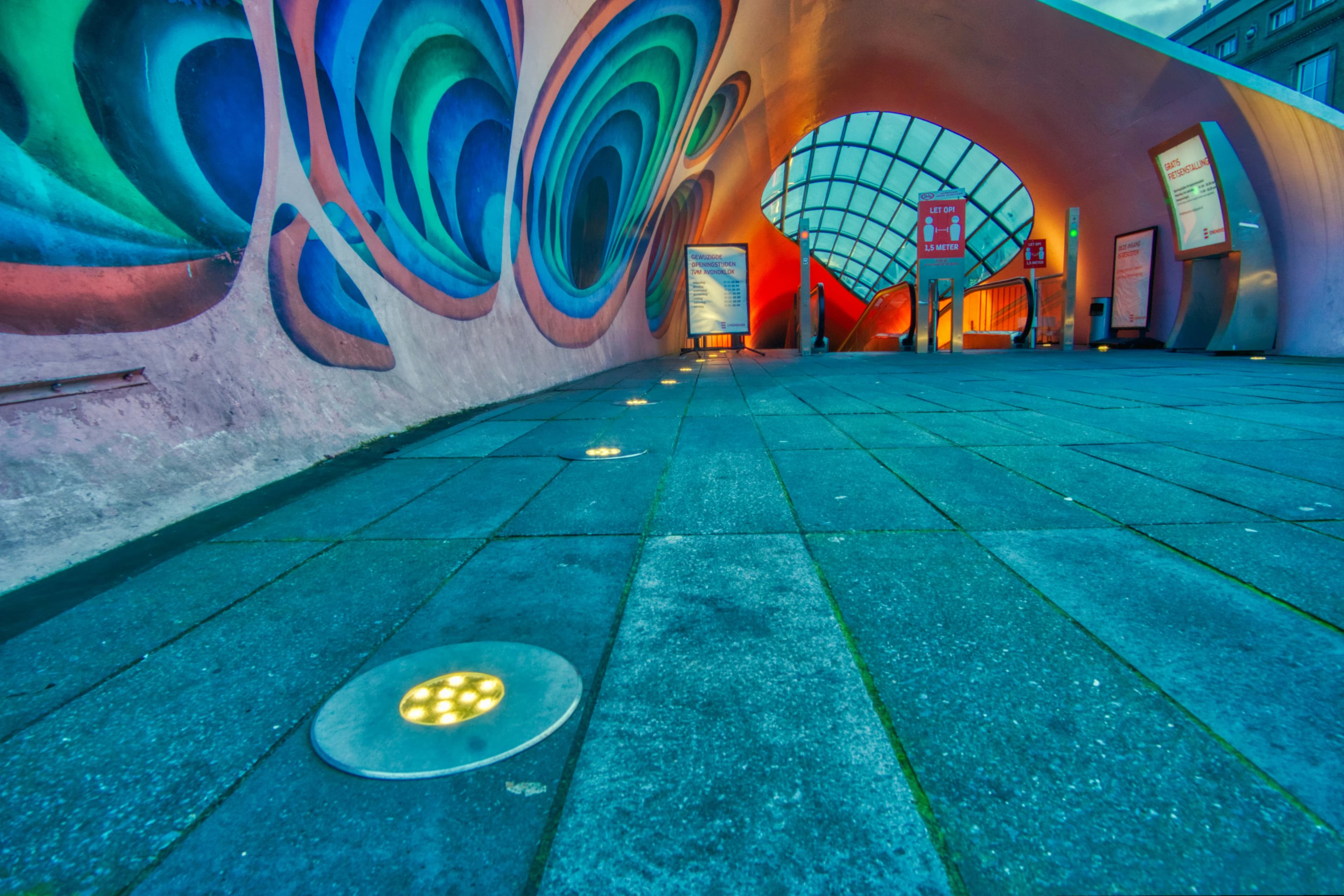 A vibrant, multicolored mural decorates an underpass, creating a striking visual as people and bicycles pass by.