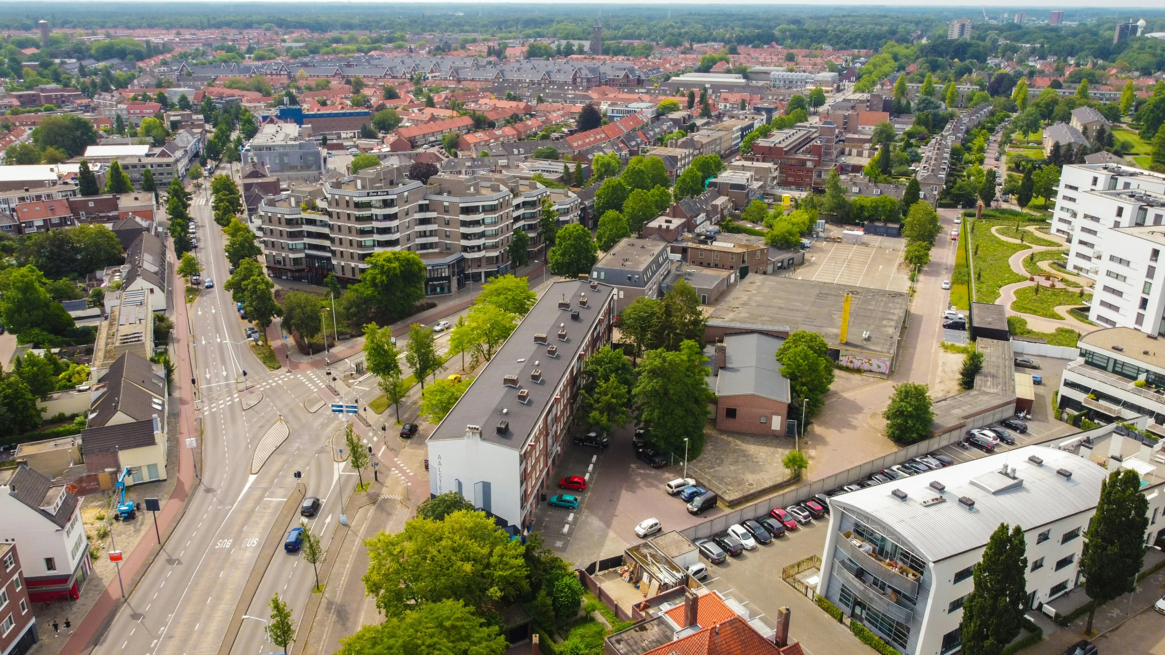 An aerial view captures the layout of Eindhoven, with a mix of modern and traditional buildings, green spaces, and a winding road.