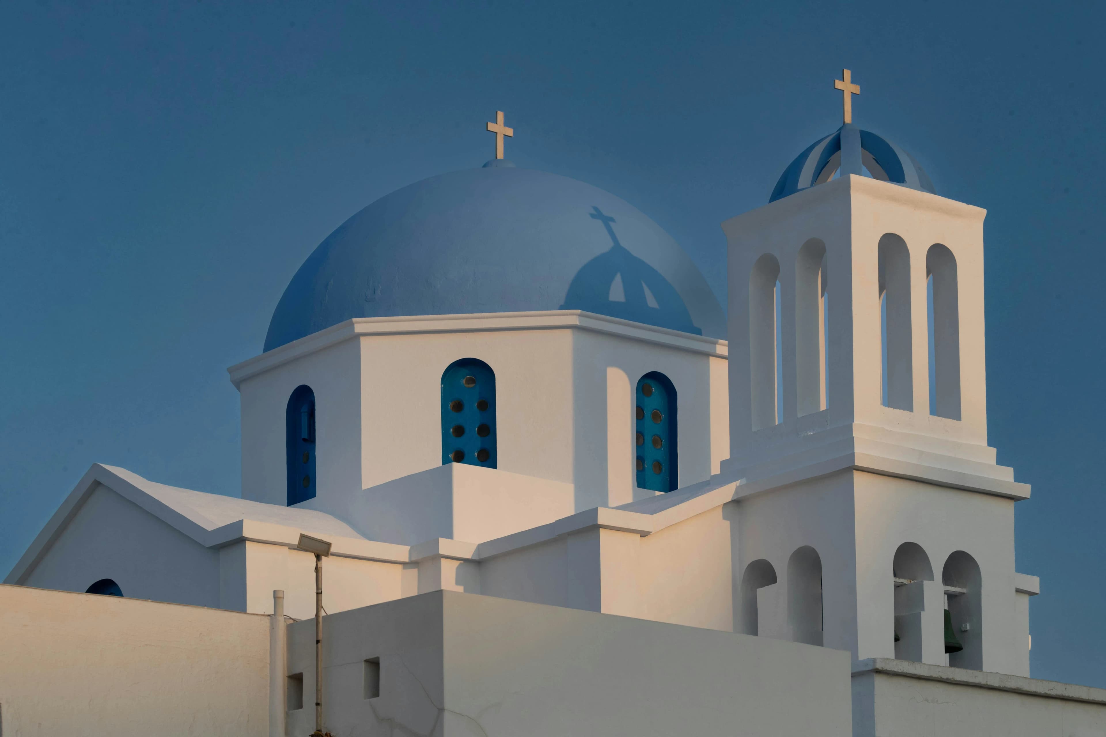 The clean, simple lines of a white church with a bright blue dome and a bell tower are a classic example of Greek island architecture.