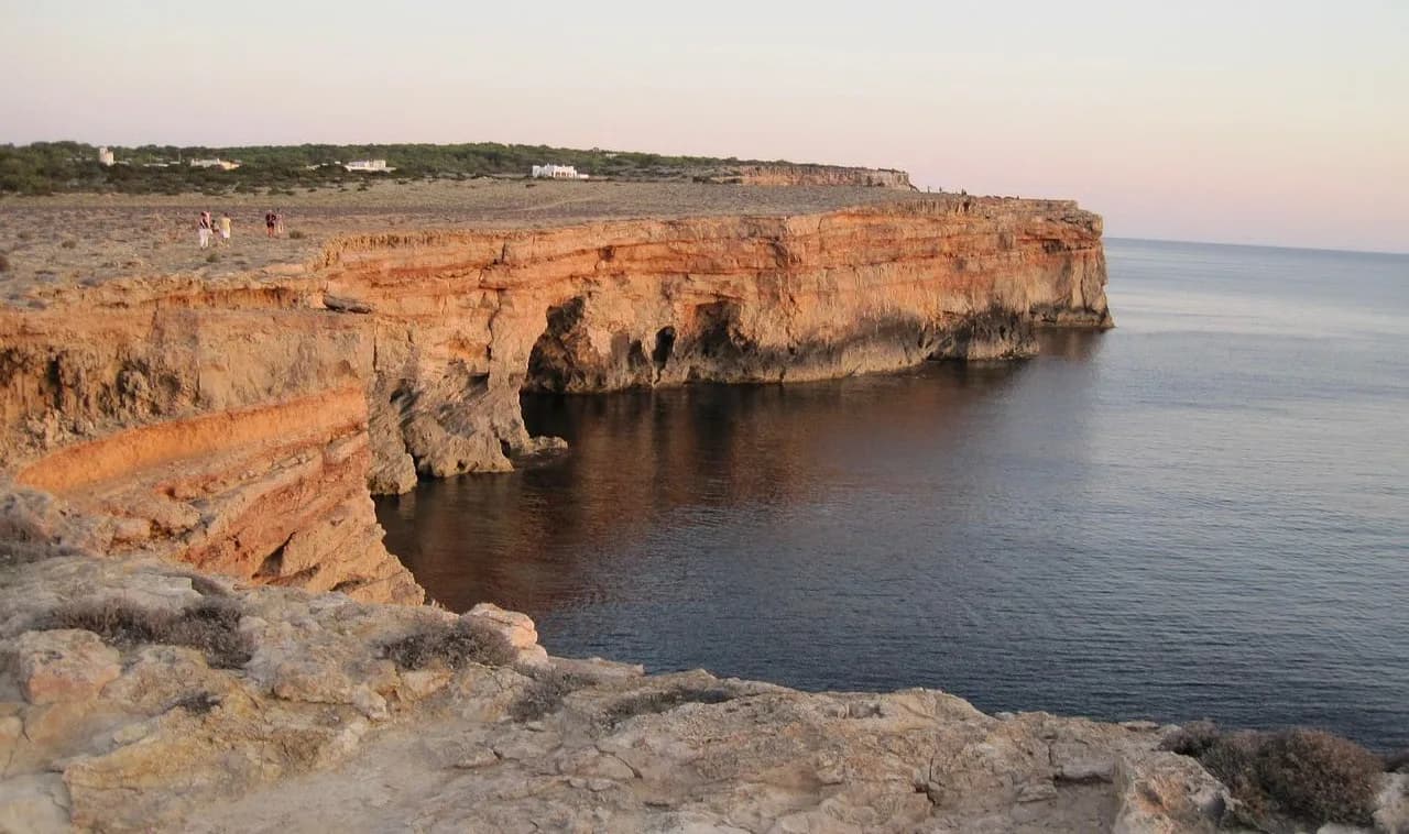 The dramatic cliffs of Formentera drop straight down into the deep blue sea, with a few people walking along the edge.
