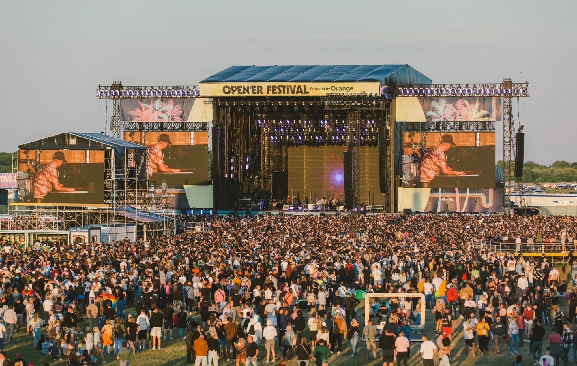 A large crowd of people gathers in front of a stage, illuminated by bright lights during the Open'er Festival in Gdynia.
