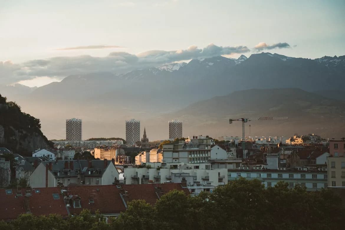 Modern towers and classic buildings are nestled in the heart of Grenoble, with the stunning snow-capped French Alps in the background.