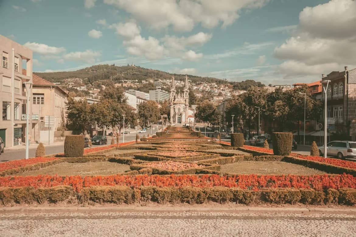 A geometric garden with colorful flowers and manicured bushes leads to a central monument in the heart of Guimarães.