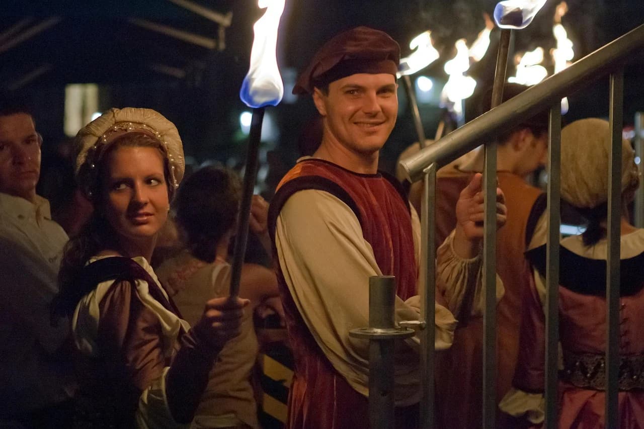 People dressed in traditional attire carry torches during a night festival, showcasing the cultural heritage of the region.