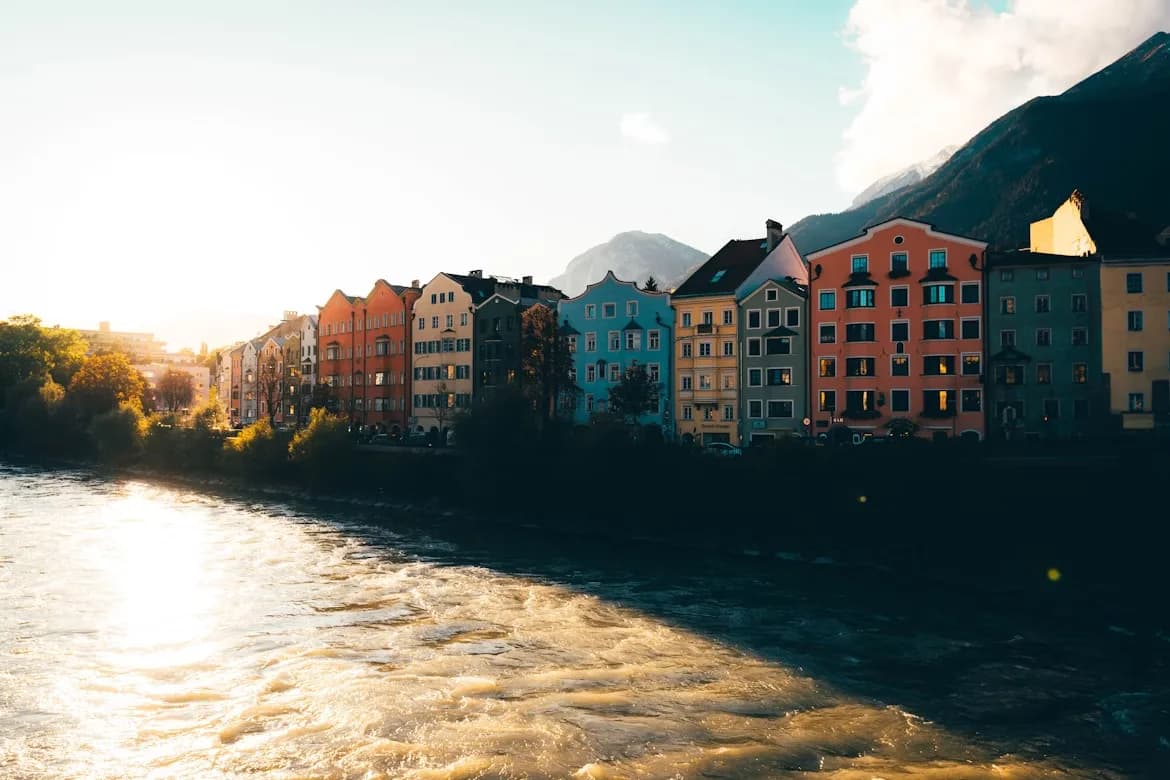 The colorful buildings of Innsbruck are reflected in the fast-flowing Inn River, with the majestic mountains rising in the background.