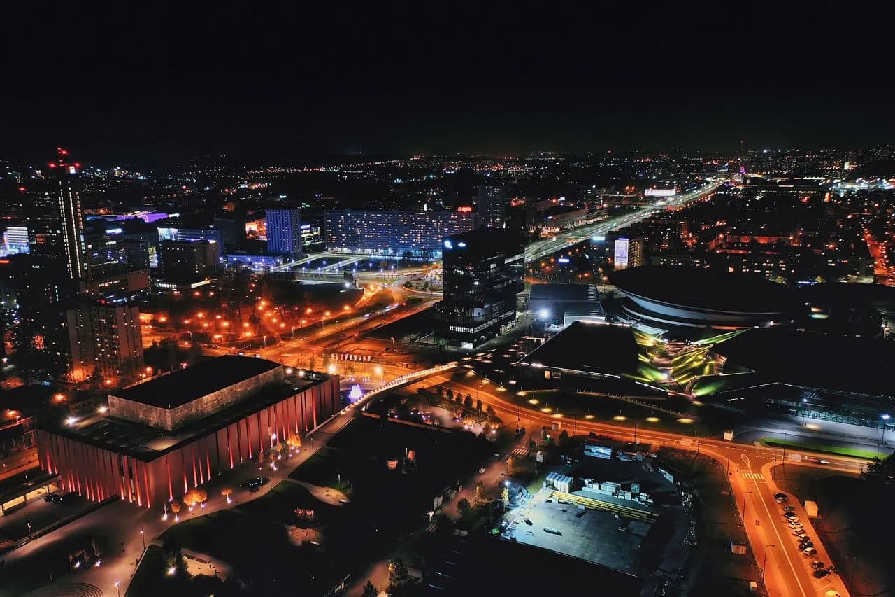 The Katowice city skyline is illuminated at night, with the bright lights of streets and buildings creating a dynamic urban landscape.