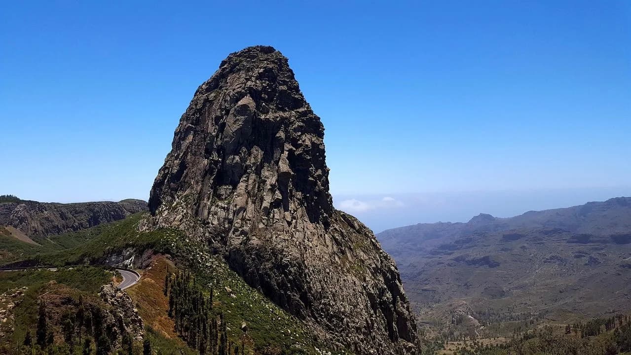 A large, towering rock formation, a natural monument of La Gomera, stands against a clear blue sky.
