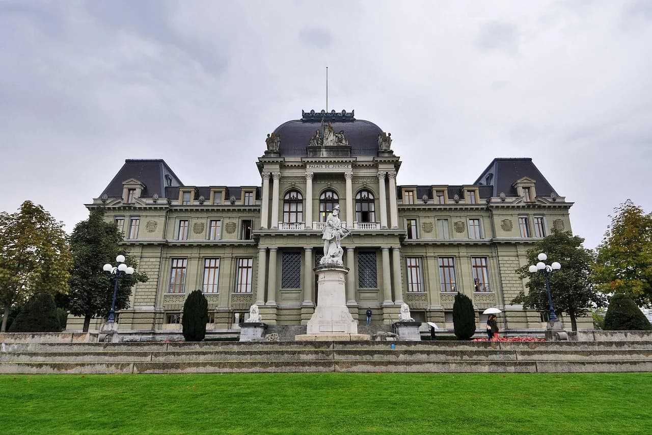 The grand facade of the Palais de Justice, a beautiful historic courthouse, is surrounded by manicured lawns.
