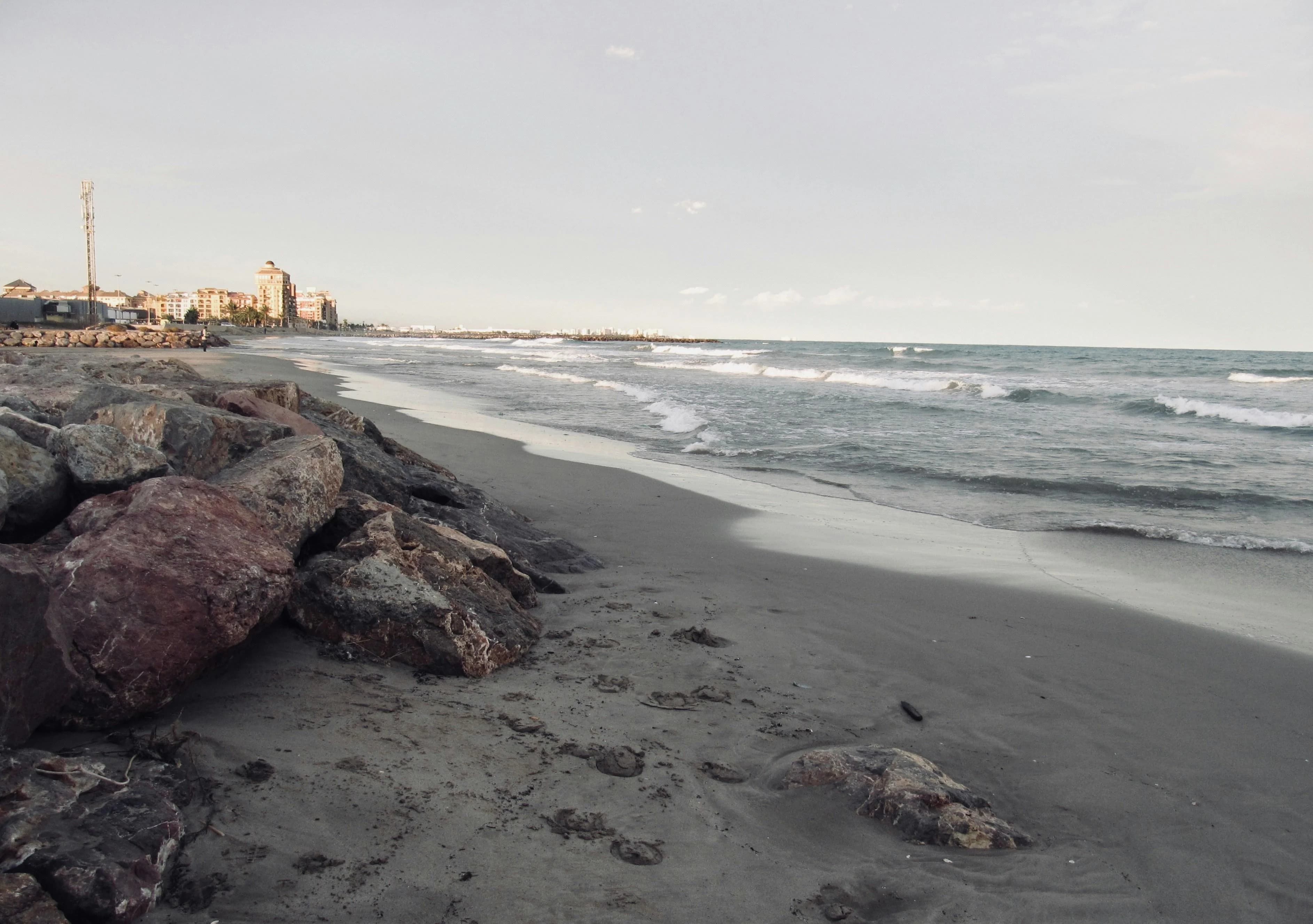 The wide, sandy beach of Le Lavandou is framed by large rocks, with gentle waves rolling toward the shore.